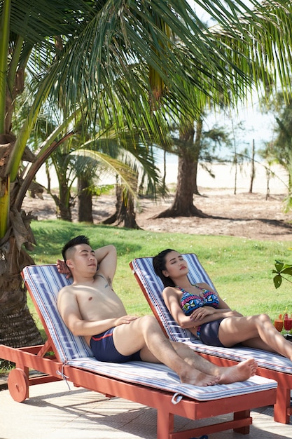 Azjatycka para relaksuje na loungers przy tropikalnym kurortem