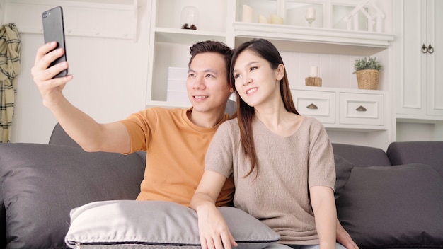 Azjatycka para używa smartphone dla selfie w żywym pokoju w domu