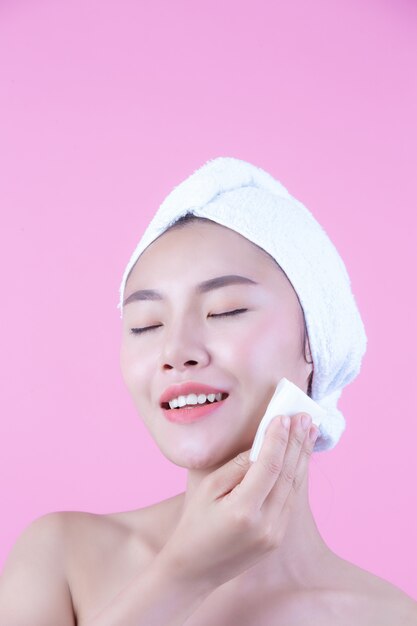 Azjatycka piękna kobieta wyciera twarz na różowym tle, kosmetologii i zdroju.