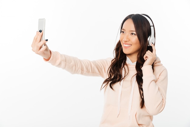 Azjatycka rozochocona kobiety słuchająca muzyka robi selfie telefonem komórkowym.