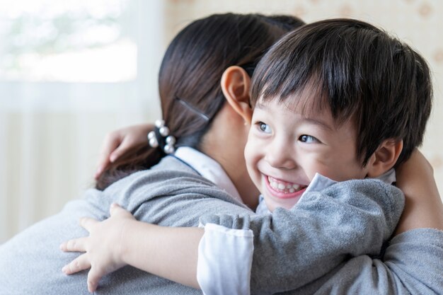 Azjatycka śliczna chłopiec ono uśmiecha się z szczęśliwie i ściska z matką w domu, rodzinny pojęcie