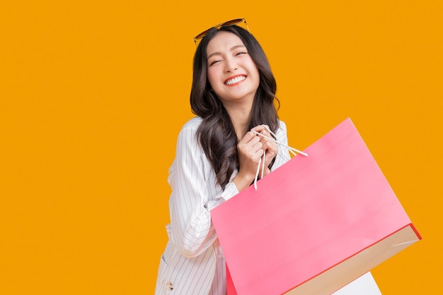 Azjatycka szczęśliwa kobieta kobieta dziewczyna trzyma kolorowe opakowania na zakupy stojąc na żółtym tle strzał studio bliska portret młoda piękna atrakcyjna dziewczyna uśmiecha się patrząc na kamery z torbami