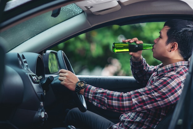 Bezpłatne zdjęcie azjatycki człowiek pije butelkę piwa podczas jazdy samochodem