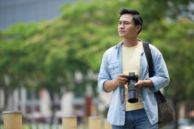 Azjatycki człowiek z profesjonalnym aparatem spacerując po parku i rozglądając się