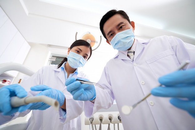 Azjatycki męski dentysta i żeńska pielęgniarka stoi above i trzyma narzędzia dla stomatologicznego egzaminu