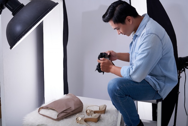 Bezpłatne zdjęcie azjatycki męski fotograf siedzi w studiu i bierze modne akcesoria zdjęcia