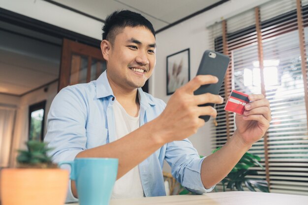 Azjatycki mężczyzna używa smartphone dla online zakupy i kredytowej karty w internecie przy żywym pokoju domem