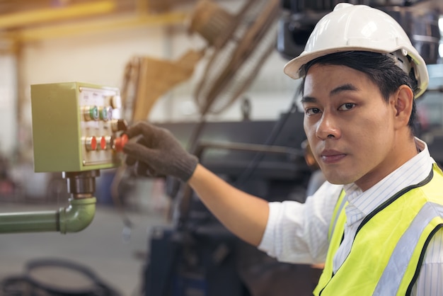 Azjatycki pracownik w kasku sprawdza maszyny w fabryce.