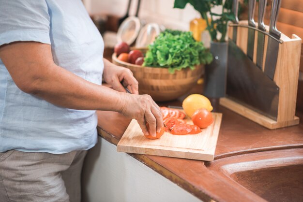 Azjatyckie starsze osoby dobierają się rżniętych pomidory przygotowywają składnik dla robić jedzeniu w kuchni