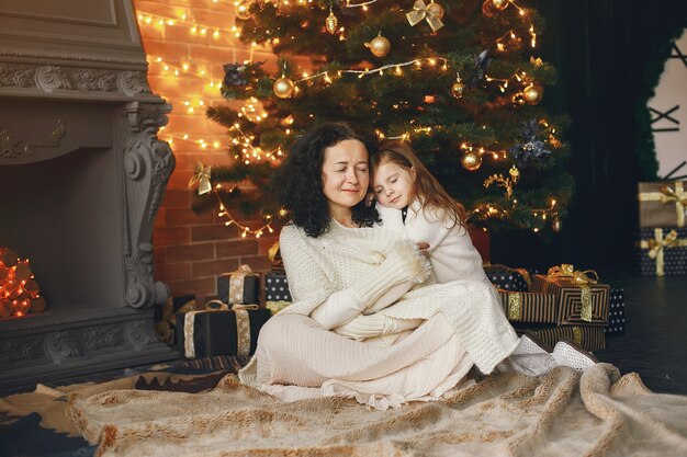 Babcia siedzi z wnuczką. Świętowanie Bożego Narodzenia w przytulnym domu. Kobieta w białym swetrze z dzianiny.