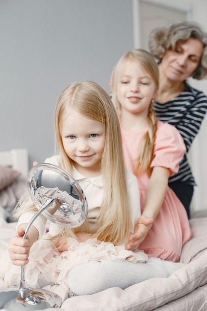 Babcia splatająca włosy wnuczki. Siostra plecionka drugiej wnuczki. Przytulny dom, relacje rodzinne.