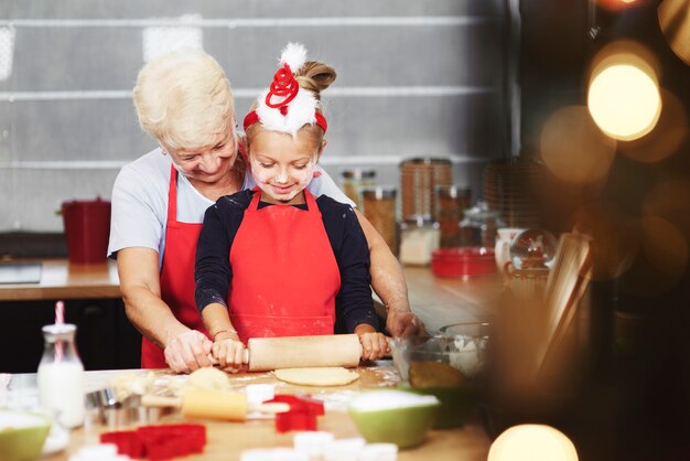 Babcia uczy wnuczkę rozwałkować ciasto