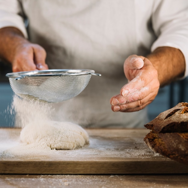 Baker przesiewa mąkę pszenną przez stalowe sito ponad wyrabianiem ciasta