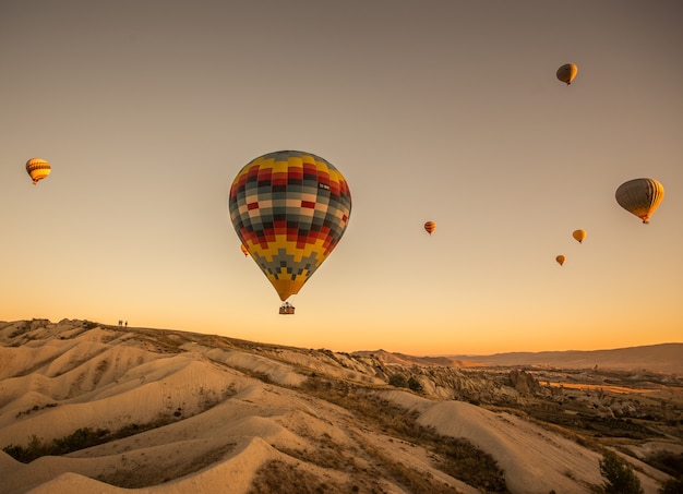 Balony na ogrzane powietrze nad wzgórzami i polami podczas zachodu słońca w Kapadocji w Turcji