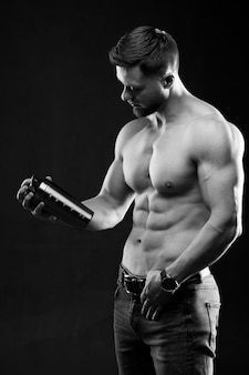 Bardzo muskularny facet sportowy trzymający napój białkowy. mężczyzna z nagim torsem. atletyczne ciało. koncepcja żywienia sportowego i sportowego. czarno-białe zdjęcie.