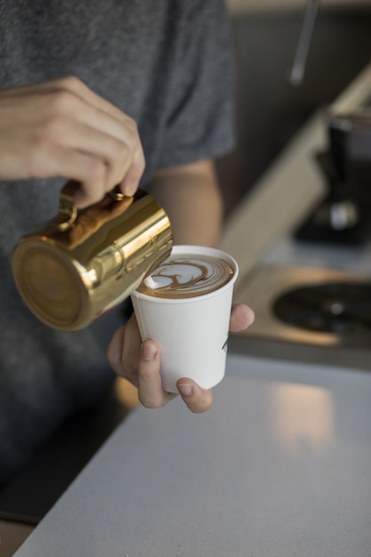 Barista nalewa śmietankę do szklanki cappuccino, tworząc piękną kawę