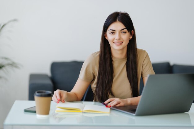 Beauitul młoda kobieta pracująca przy użyciu komputera przenośnego skoncentrowana i uśmiechnięta w domowym biurze