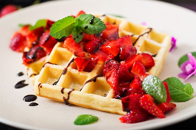 Belgia wafle z truskawkami, czekoladą i syropem na talerzu.