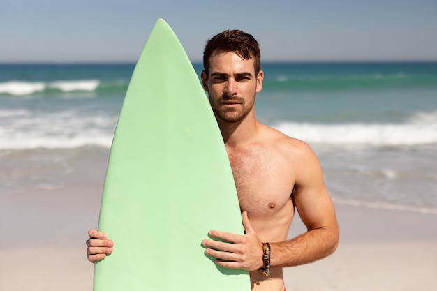 Bez koszuli mężczyzna patrzeje kamerę na plaży w świetle słonecznym z deską surfingową