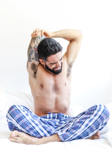Bezpłatne zdjęcie bez koszuli młody człowiek rozciąga jego ręki na łóżku