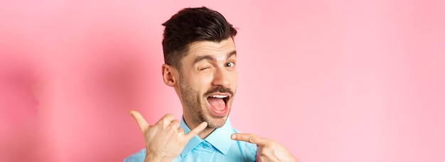 Bezpłatne zdjęcie bezczelny i zabawny facet pokazujący gest telefonu z prośbą o telefon i mrugający, mówiący o wybraniu numeru st