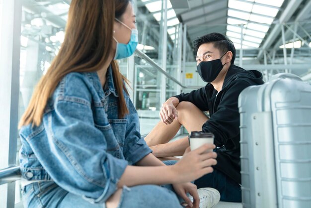 Bezpieczne podróże nowy normalny styl życia azjatycka przyjaciółka para zrelaksuj się, usiądź, poczekaj na harmonogram, aby wejść na pokład azjatyckiego mężczyzny i kobiety noszących maskę ochronną w terminalu lotniska