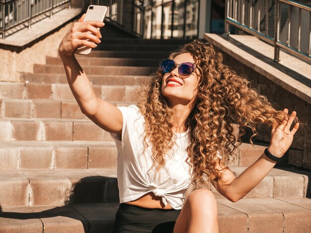 Beztroska dziewczyna siedzi na schodach na ulicy, biorąc selfie