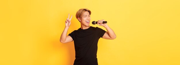 Beztroski przystojny azjatycki facet wykonujący piosenkę śpiewającą do mikrofonu i pokazujący gest pokoju