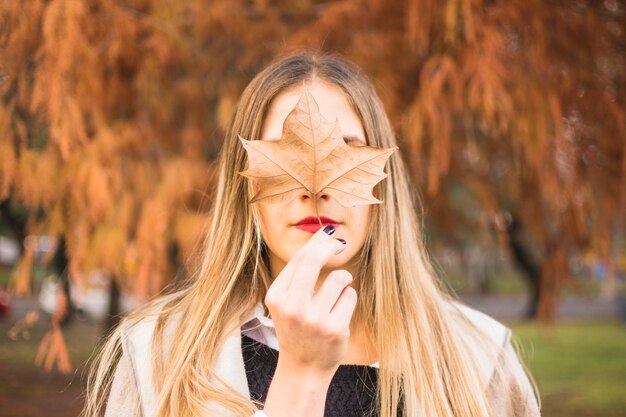 Beztwarzowy blond kobiety mienia liść na twarz