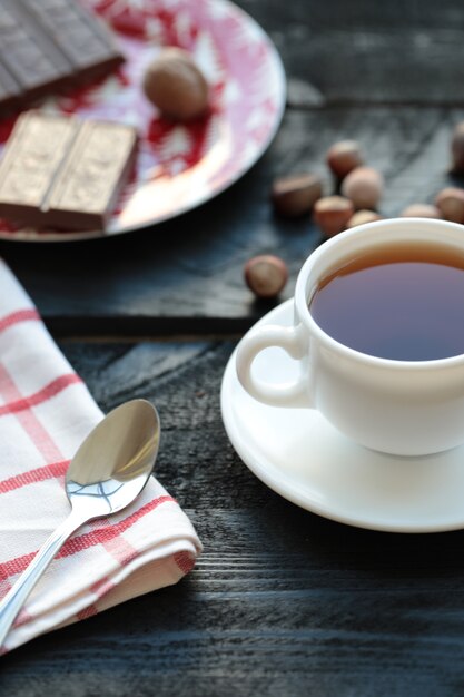 Biała filiżanka herbaty z tabliczką czekolady na drewnianym stole.