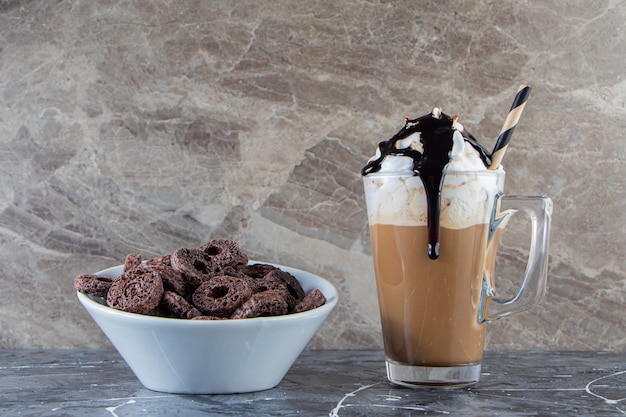 Biała miska płatków czekoladowych i szklanka kawy na marmurowej powierzchni.