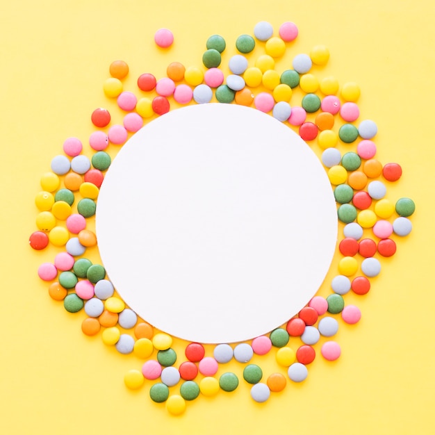 Bezpłatne zdjęcie biała pusta rama otaczająca z kolorowymi klejnotów cukierkami na żółtym tle