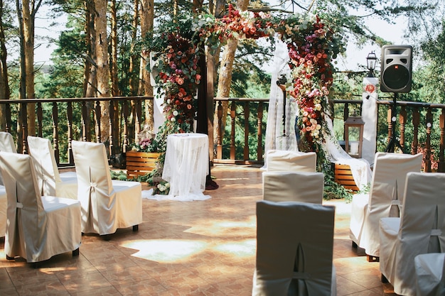 Białe krzesła stoją przed ołtarzem weselnym na ganku
