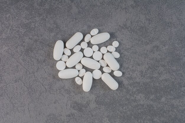 Białe tabletki medyczne na marmurowym stole.