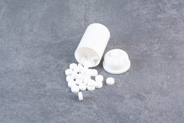Białe tabletki medyczne z plastikowego pojemnika.