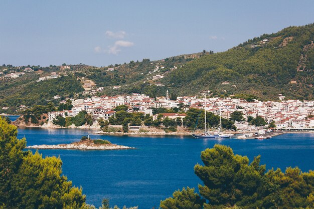 Biali i brown domy zbliżają błękitnego ocean otaczającego górami z drzewami w Skiathos, Grecja