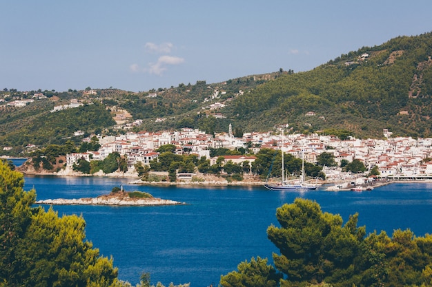 Biali i brown domy zbliżają błękitnego ocean otaczającego górami z drzewami w Skiathos, Grecja