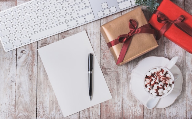 Biały papier, klawiatury komputera, prezent na Boże Narodzenie i kubek z marshmallows