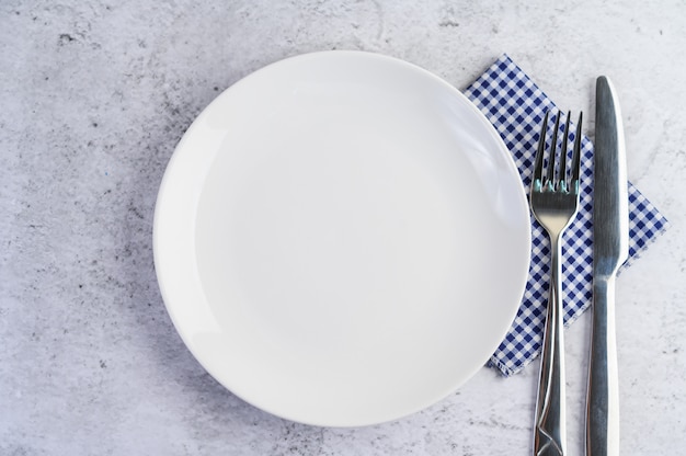 Biały pusty talerz z widelcem i nożem na niebiesko-białym obrusie.