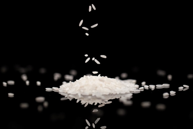 Biały ryż spada na czarnym szklanym stole w ciemnym pokoju
