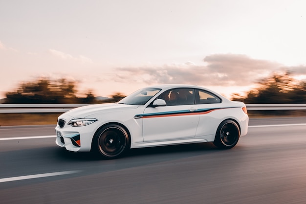 Biały sportowy sedan z kolorowym tuningiem na drodze.