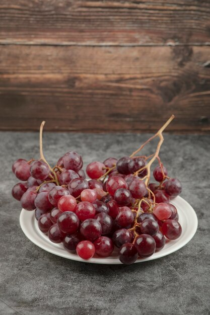 Biały talerz i czerwone pyszne winogrona na marmurowym stole.