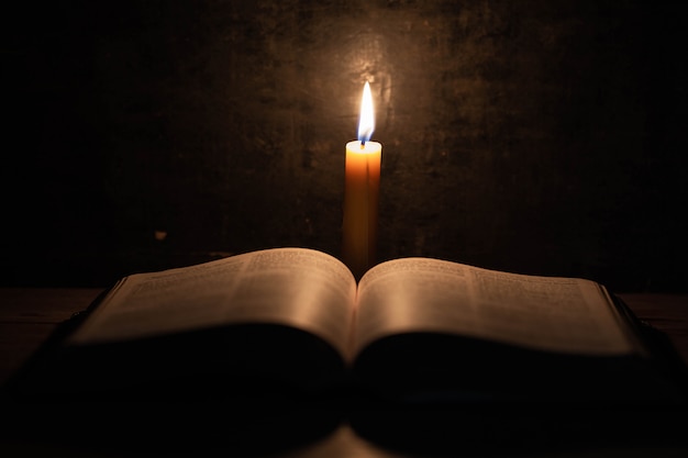 Biblia i świeca na starym dębowym drewnianym stole.
