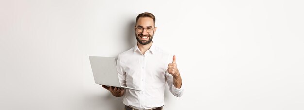 Biznes młody udany mężczyzna przedsiębiorca pokazując kciuk podczas pracy na laptopie stojąc nad kim