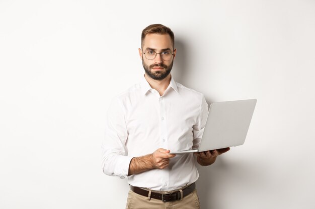 Biznes. Przystojny menedżer pracuje na laptopie, trzymając komputer i patrząc na kamery, na stojąco