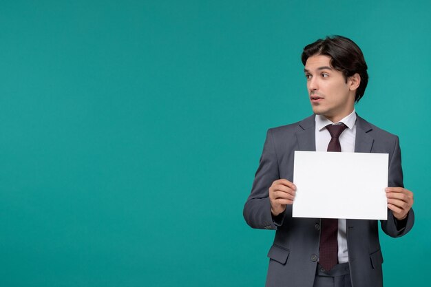 Biznesmen ładny przystojny facet w szarym biurowym garniturze i krawacie, patrząc w lewo, trzymając papier