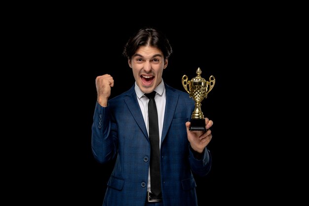 Biznesmen młody podekscytowany przystojny facet w ciemnoniebieskim garniturze z krawatem trzymającym trofeum