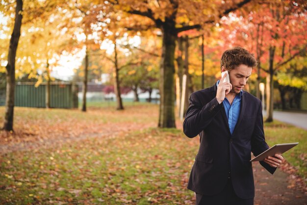 Biznesmen opowiada na telefonie komórkowym i trzyma cyfrową pastylkę