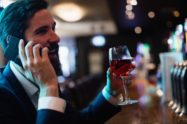 Biznesmen opowiada na telefonie komórkowym podczas gdy mieć szkło wino