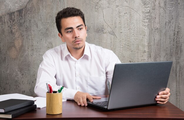 Biznesmen, patrząc na laptopa i siedząc przy biurku. Wysokiej jakości zdjęcie